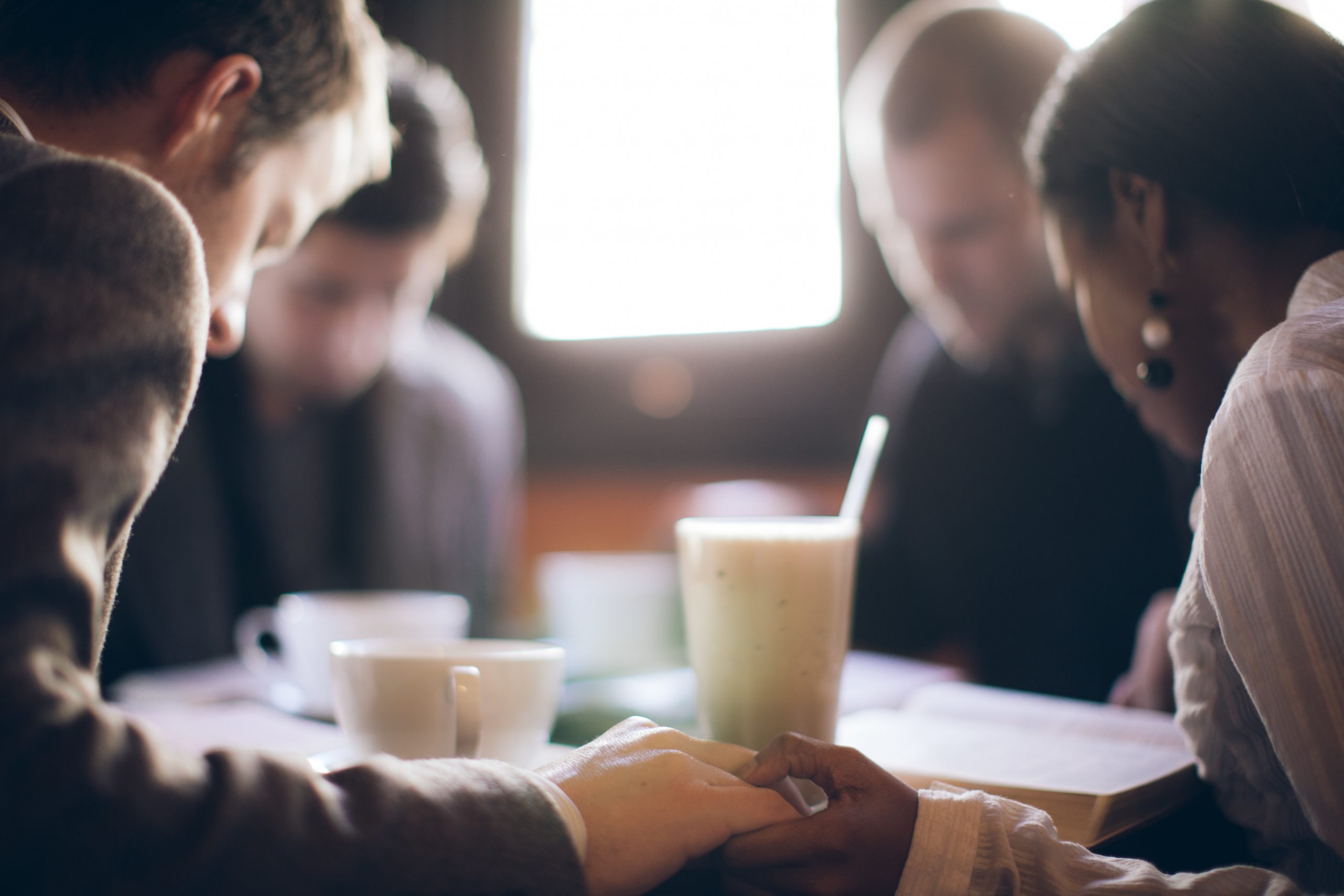 blurred image of four adults gathering in prayer around a table with beverages