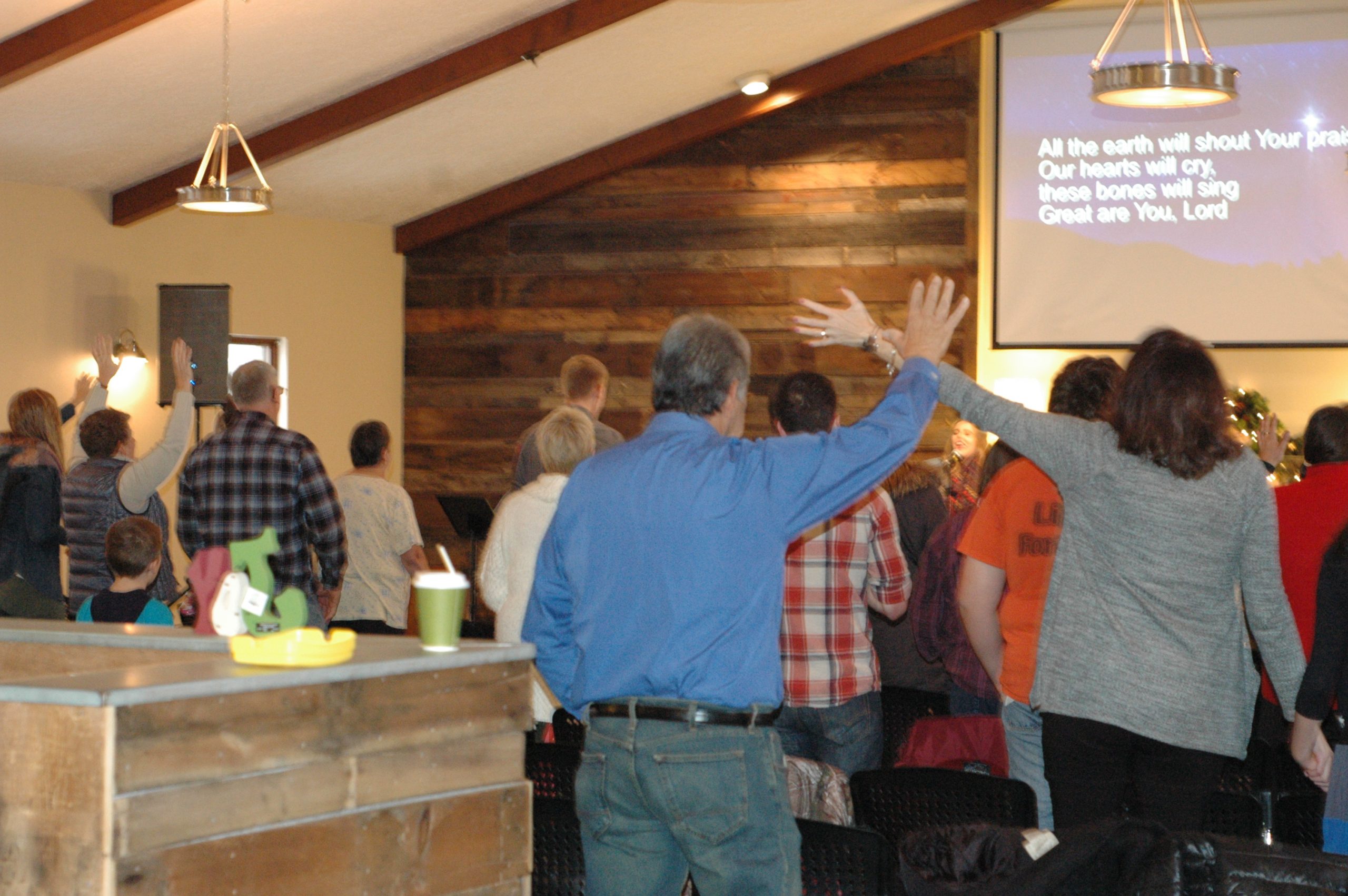 As pessoas se reúnem em uma pequena igreja para adoração, algumas com as mãos erguidas.