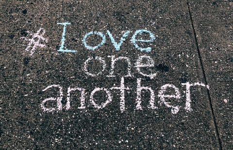 Love one another is written in chalk on the sidewalk.
