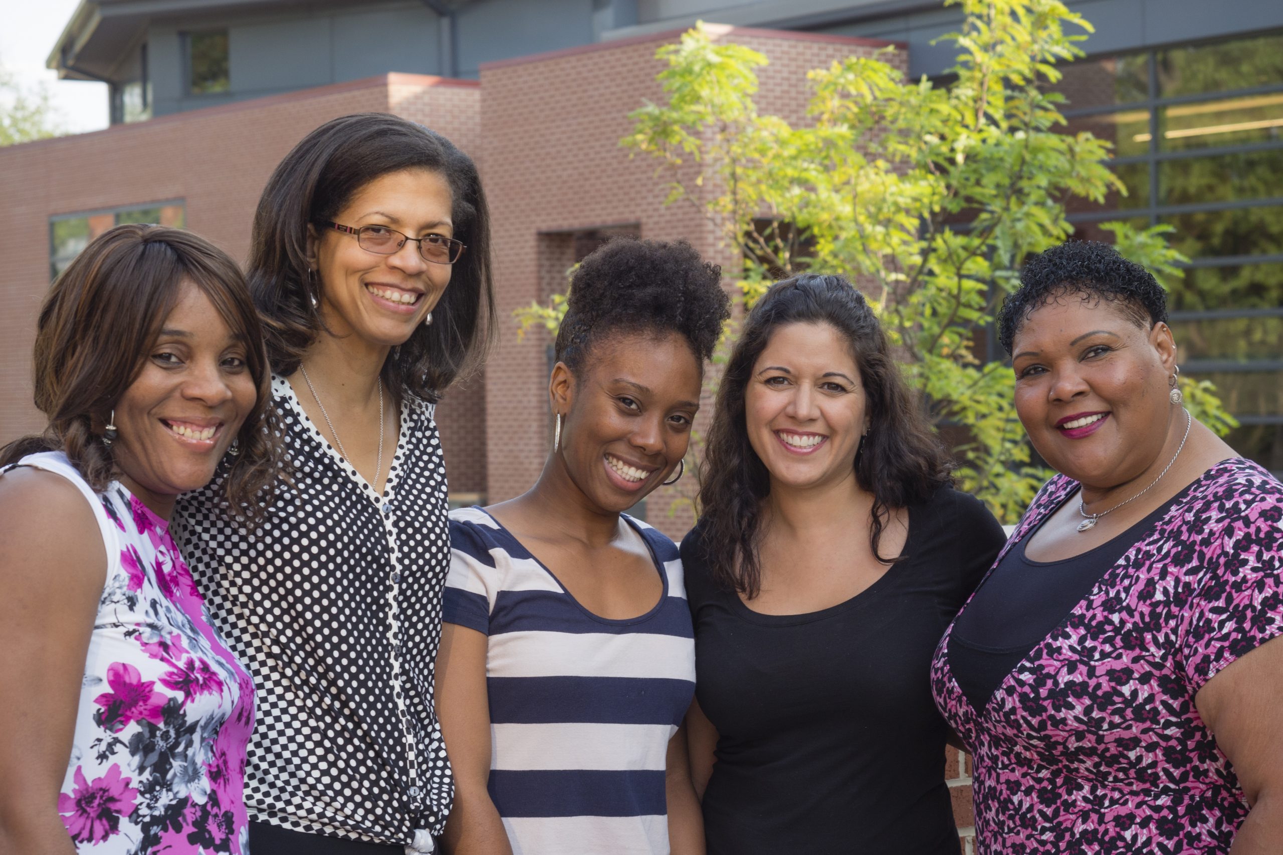 Un grupo de cinco mujeres sonríe y posa frente a un edificio.