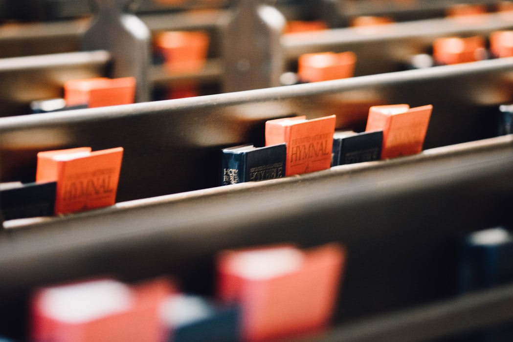 Bíblias pretas e hinários vermelhos alinham as costas dos bancos da igreja.