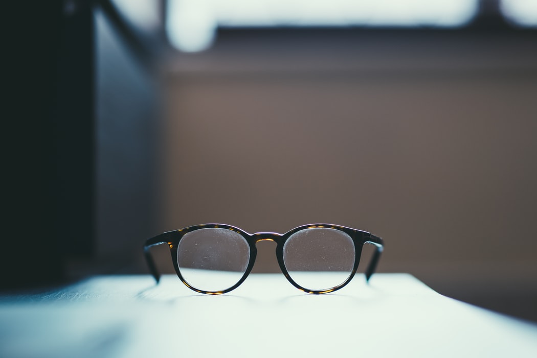 A pair of tortoise shell glasses sit on a table against a blurry background.