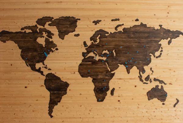 A world map, made of wood, contains blue push pins in various locations.