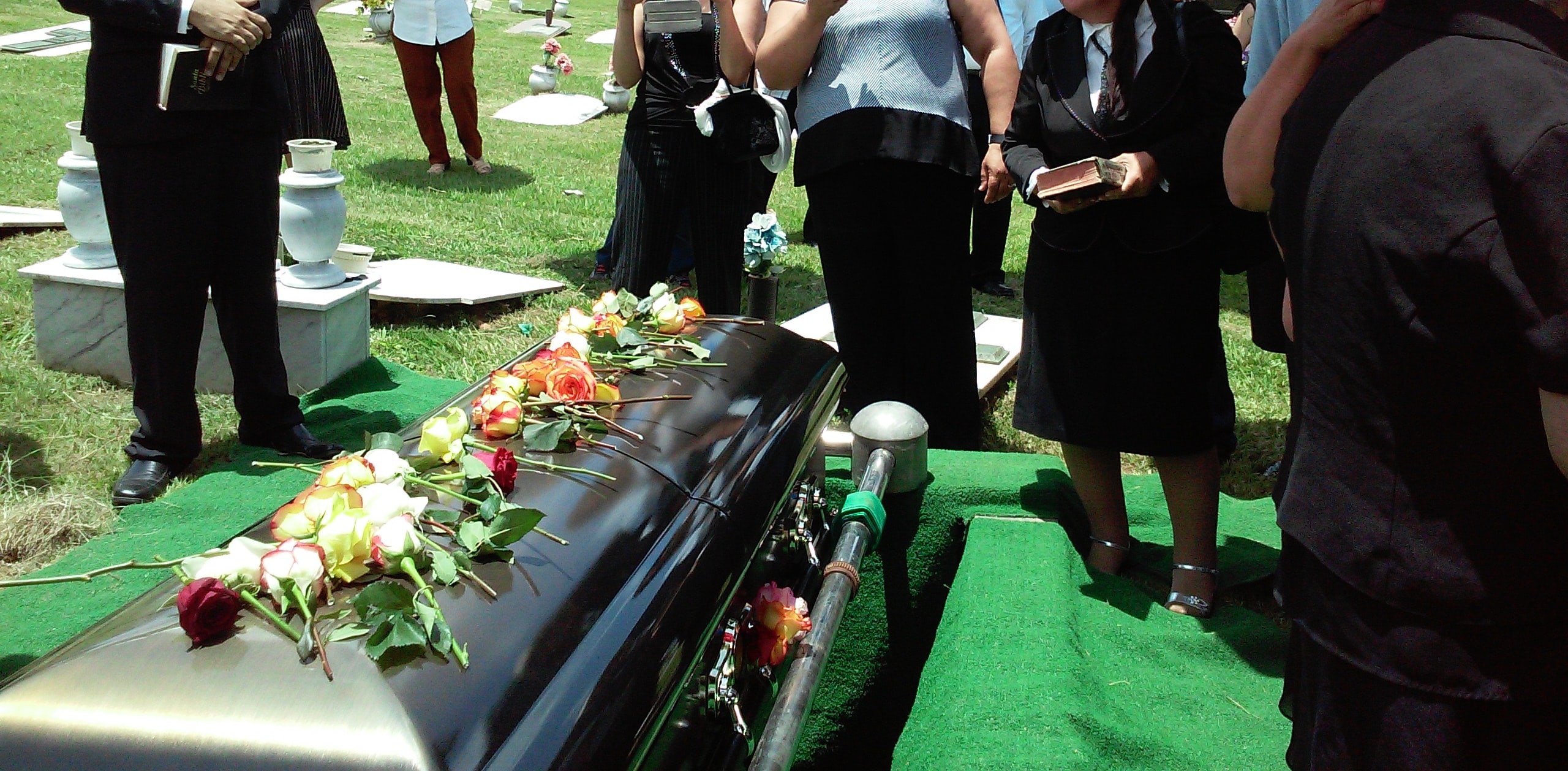 People dressed in black gather around a casket with flowers prepared for burial.